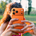 AGL10645 - iPhone 17 Pro Optik Pro XL EZ Fit Lens Protector in orange showing a person holding the case with both hands